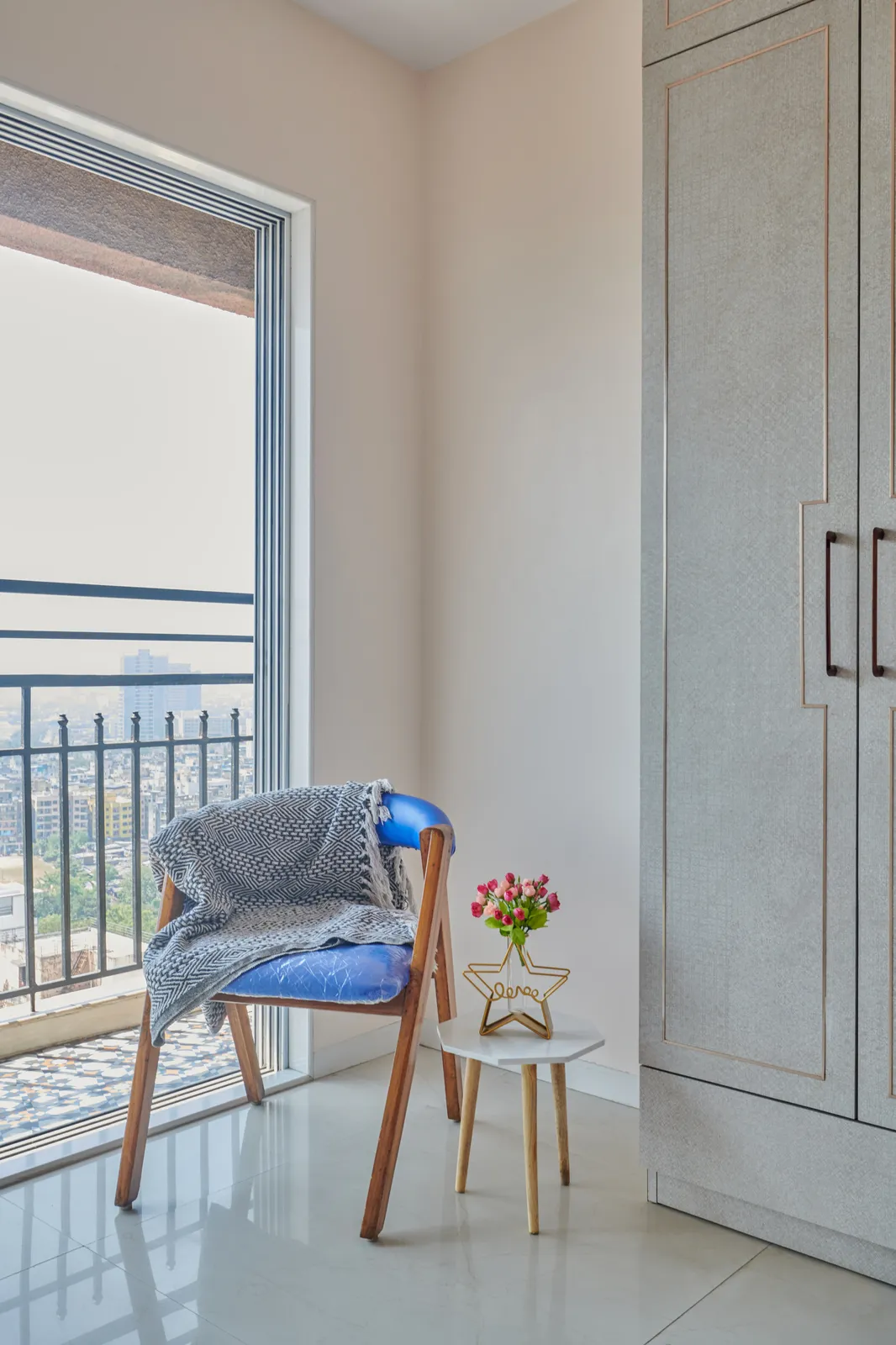 A cozy corner by the balcony in Bedroom 1, featuring a blue accent chair and a small side table, perfect for enjoying the cityscape view