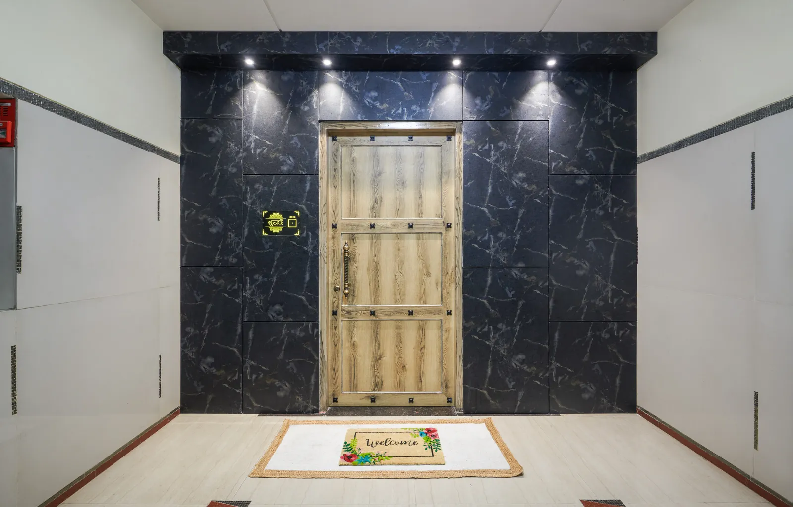 A warm welcome awaits at the entrance of this Koper Khairane 2 BHK, featuring a rustic-chic wooden door and sleek black marble-finish walls.