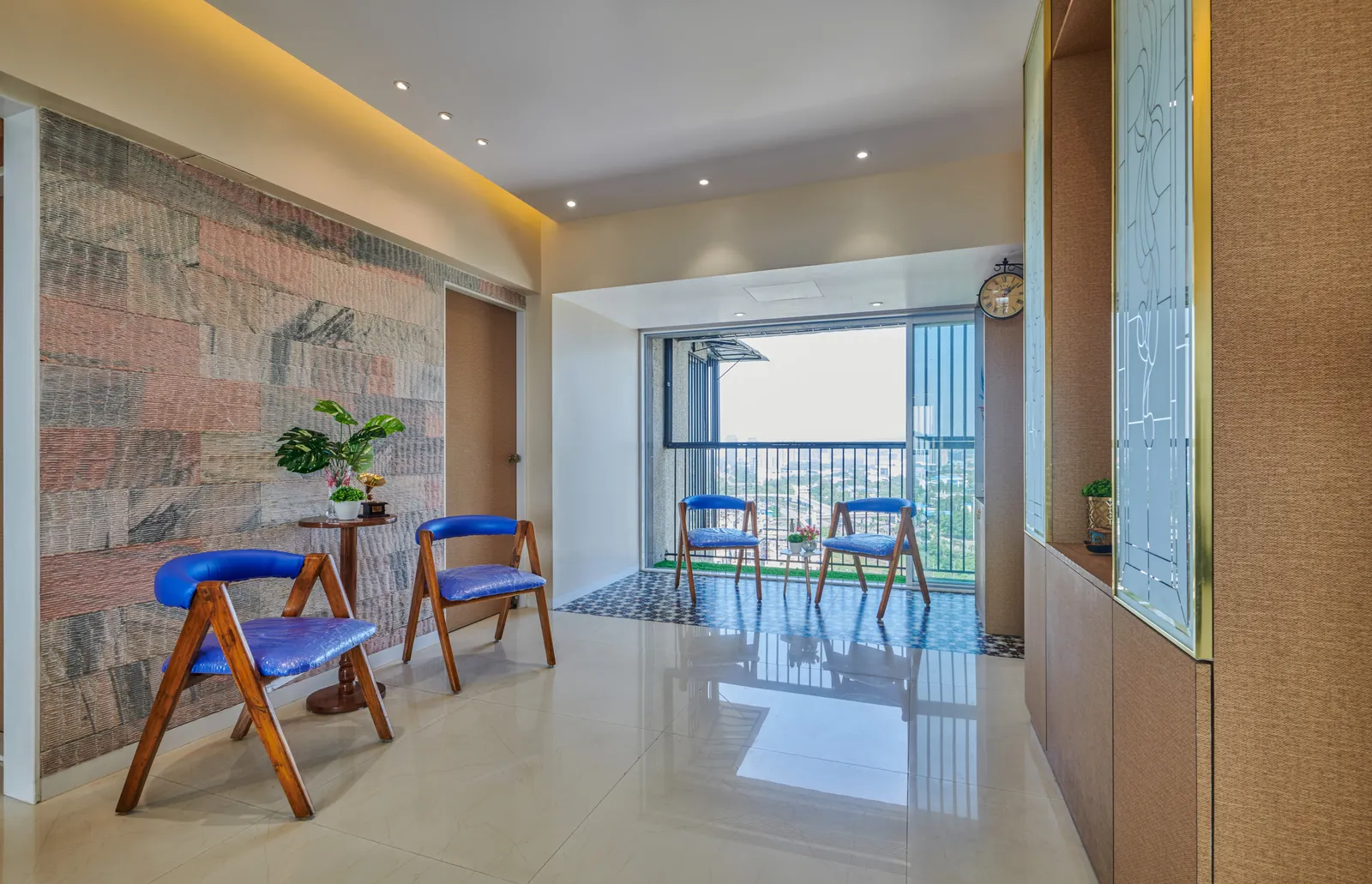 Vibrant blue accent chairs and a side table create a functional passage leading to the balcony, maintaining visual continuity throughout the space.